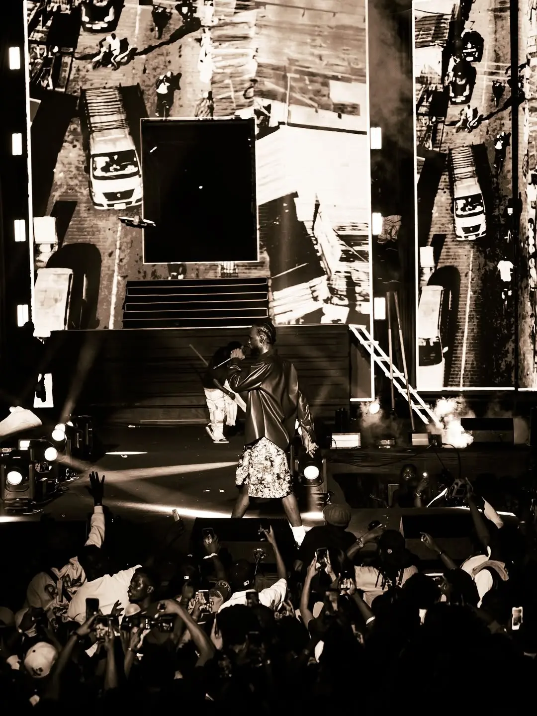 Artist performing in front of giant black-and-white screens as the crowd reaches up