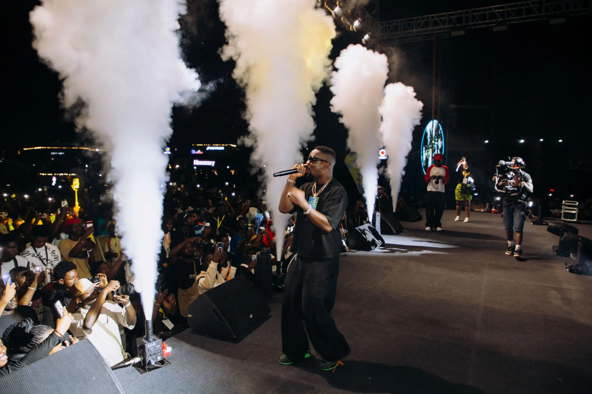 Artist performing between CO2 jets in front of a packed crowd filming on their phones